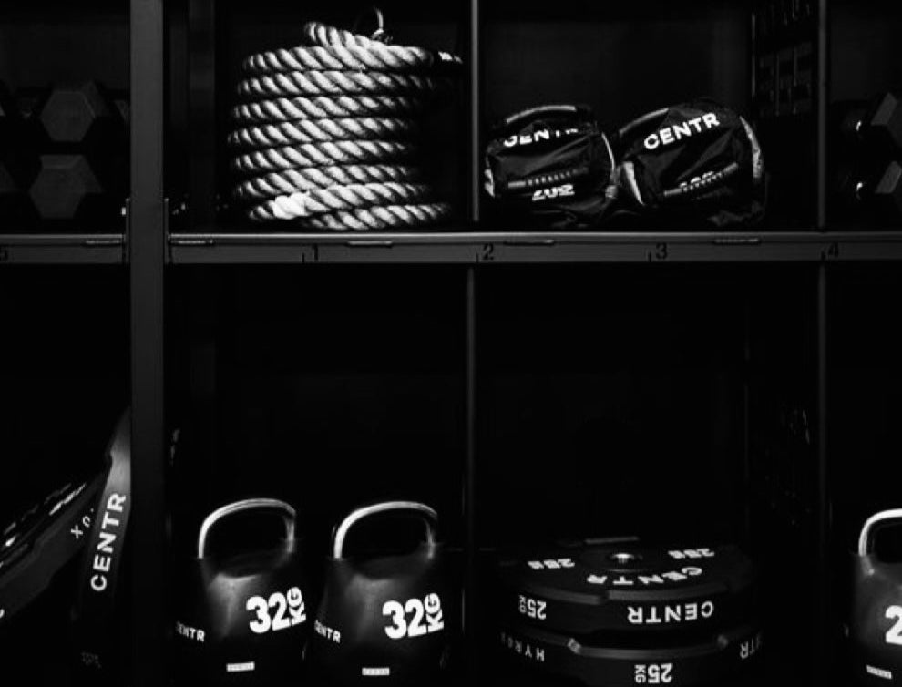 Black and white gym equipment including ropes, kettlebells, and weights on a shelf.
